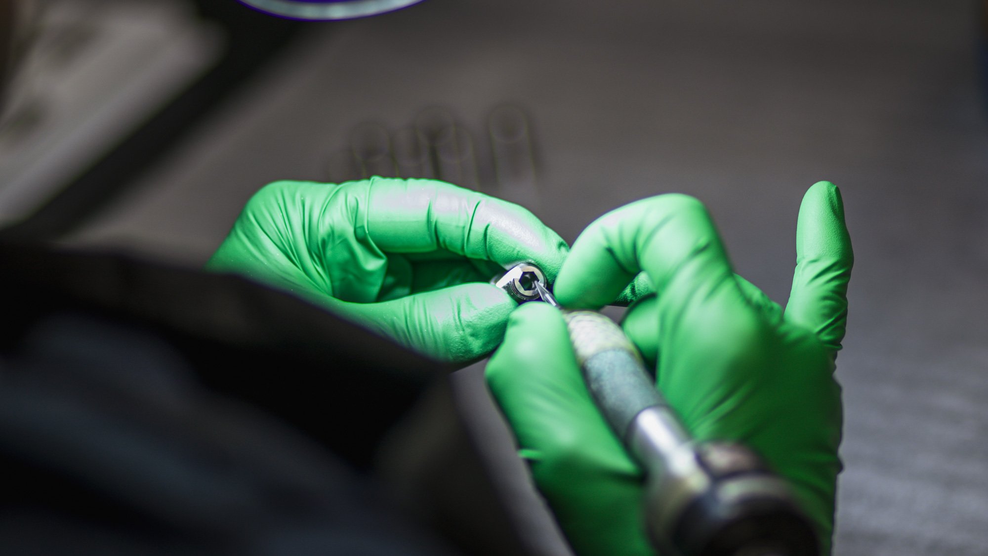 Gloved hands handling a small hex bolt with a wrench or socket tool