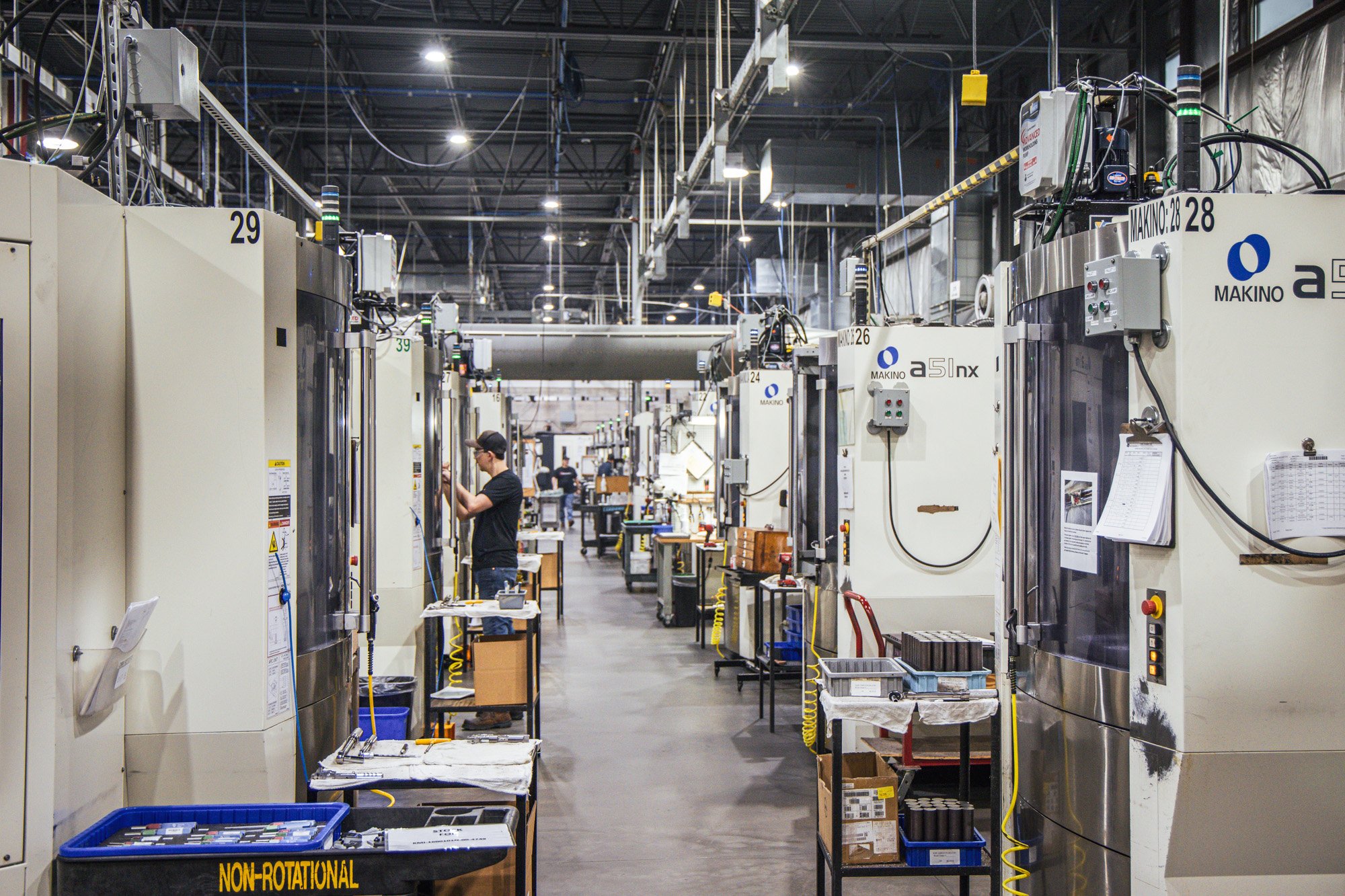 A technician operating CNC equipment in a large facility lined with machining centers.