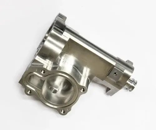CNC-machined aluminum throttle body or intake manifold housing with circular bore, mounting flanges, and machined ports, on white background.