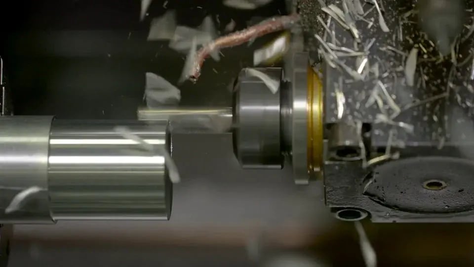 Close-up of a metal part being turned on a lathe with metal chips flying from the cutting tool.