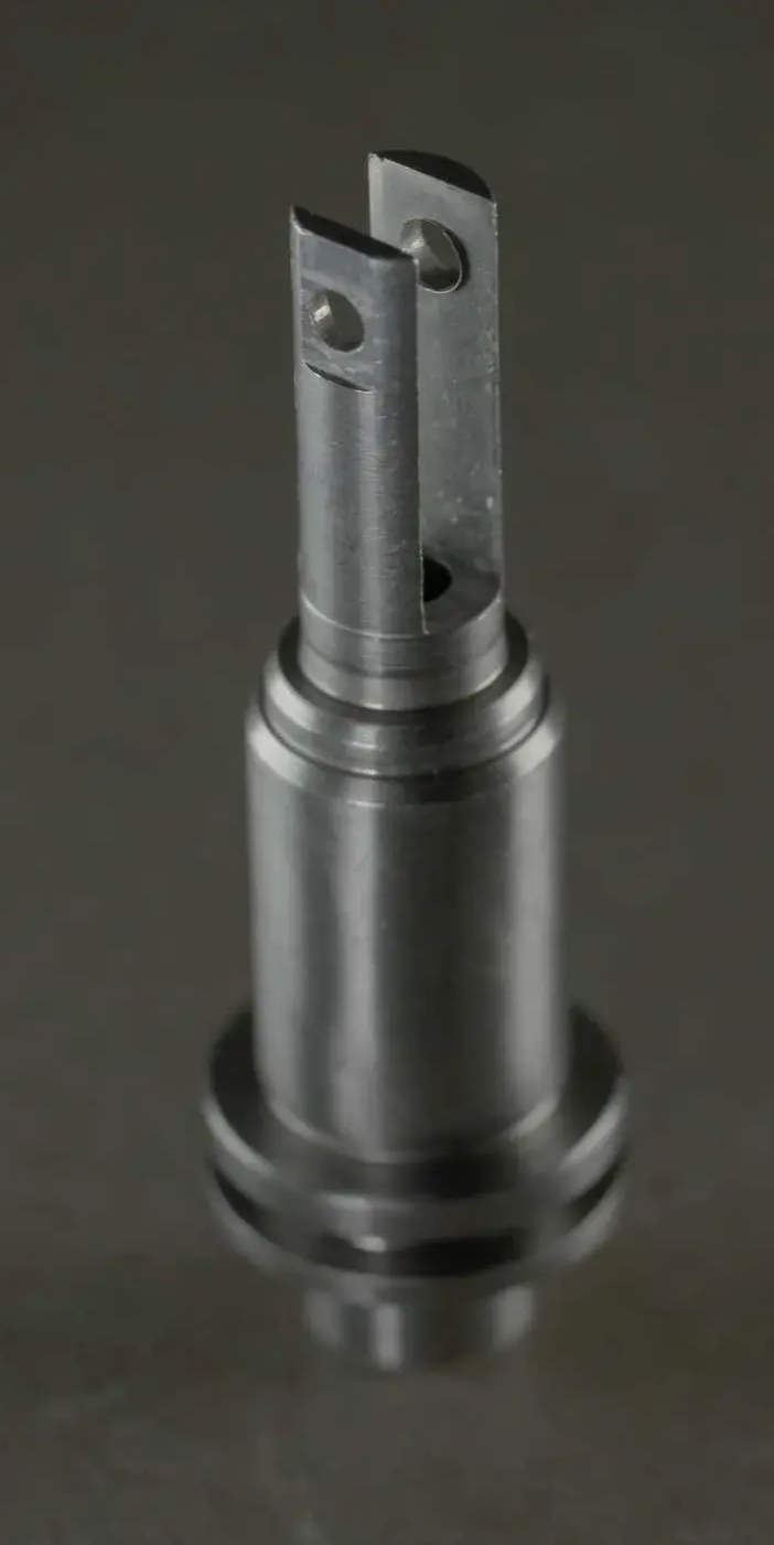 A close-up studio shot of a small precision machined cylindrical metal component with a slotted tip.