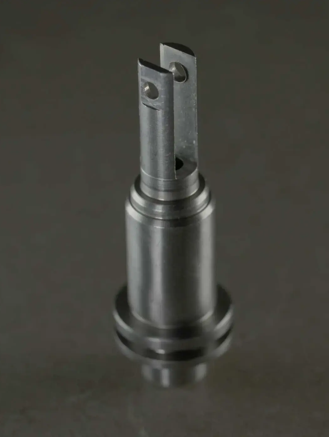 A close-up studio shot of a small precision machined cylindrical metal component with a slotted tip.