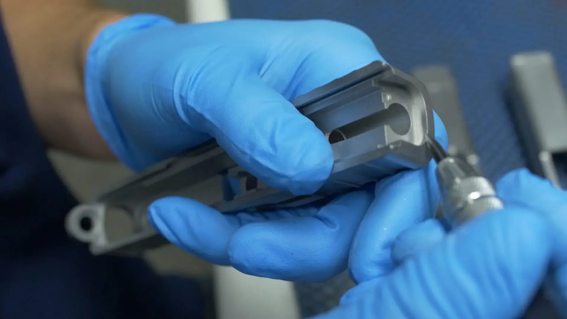 Gloved hands carefully handling a precision machined metal component during inspection or assembly.