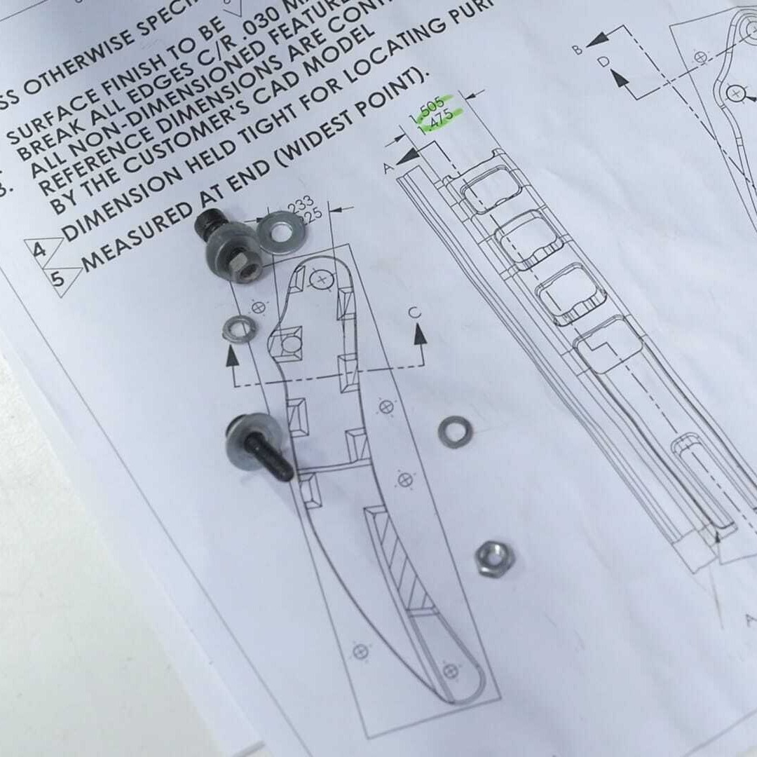A precision machined part placed on top of a detailed engineering drawing for reference.