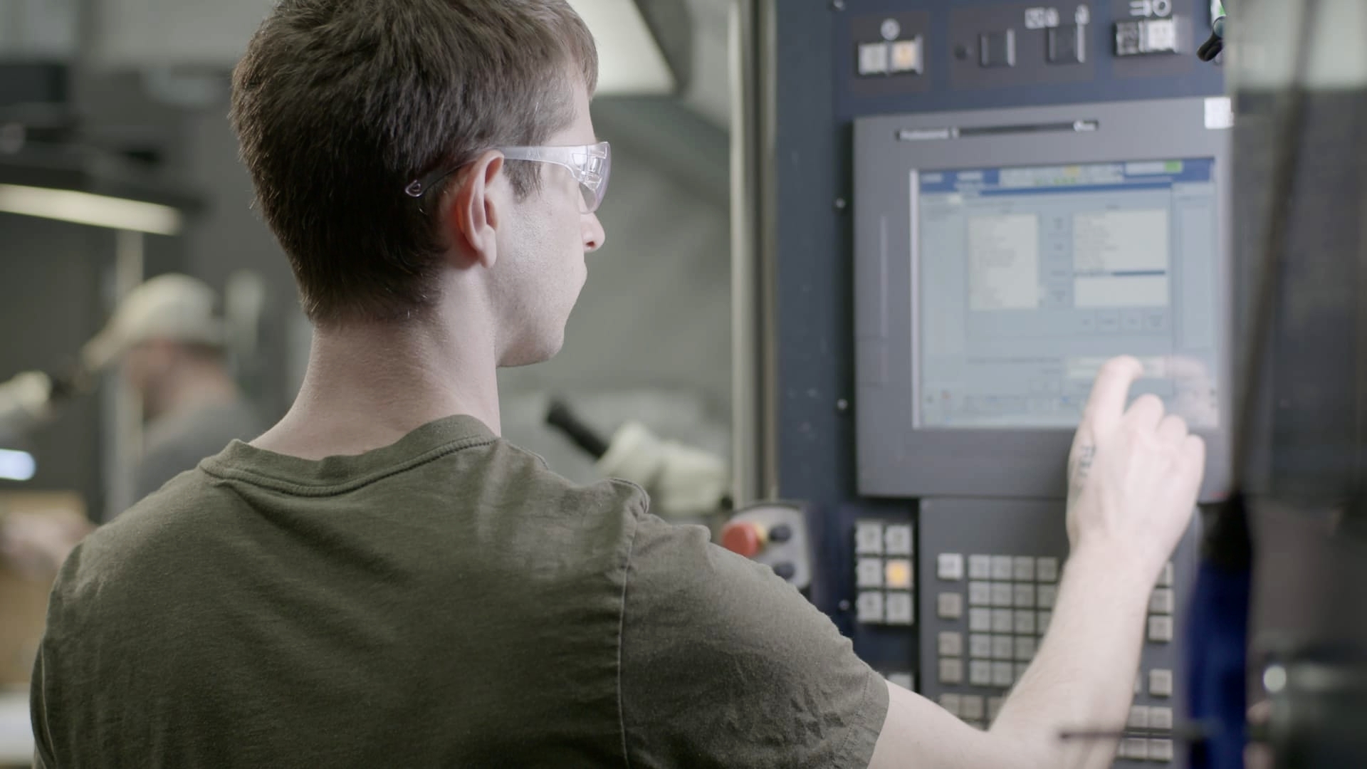 A machinist wearing safety glasses entering a program into a CNC machine control panel.