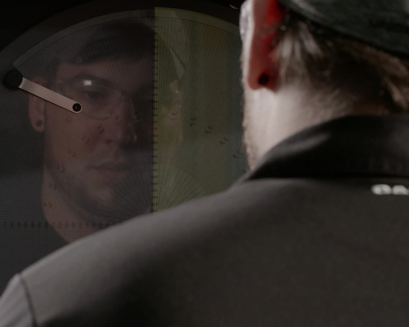 A machinist closely examining a precision measurement gauge in a dimly lit inspection area.