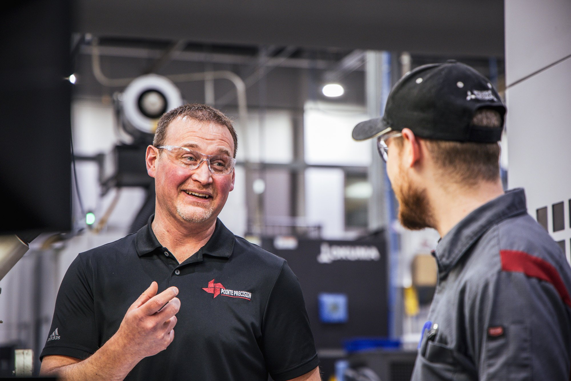 Two Pointe Precision employees in conversation on the manufacturing floor.